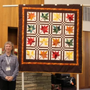 The Maple Leaf pattern is from the August BBQ Quilters Runway pattern on this website. She paper pieced it from scraps in her stash. It will be donated by her church to refugees living in Boise.